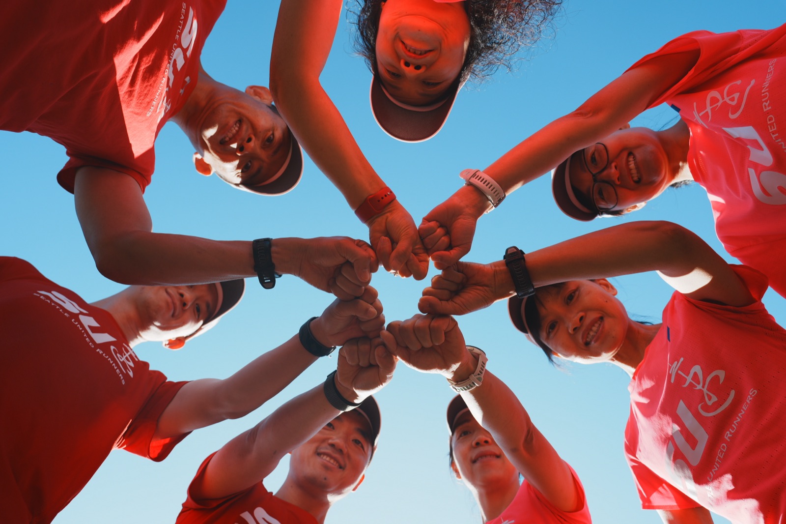 Seattle United Runners teammates joining hands in a circle under a blue sky